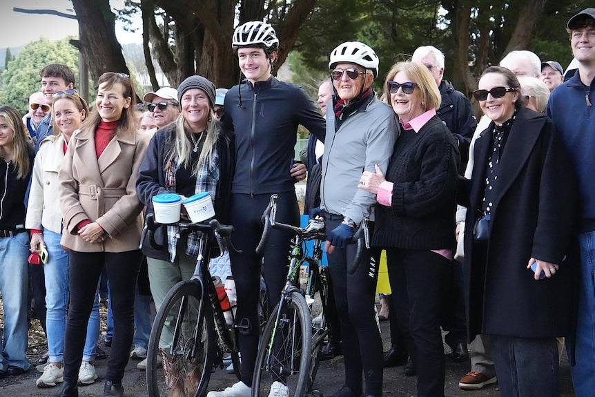 Group of people smiling with two men holding bikes.