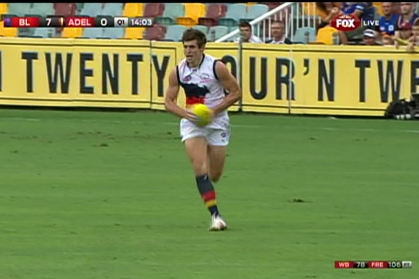 A man in a footy uniform runs across a green oval holding a yellow football