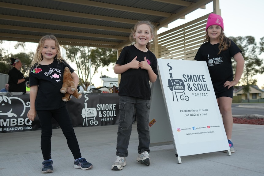 Three young girls stand next to a Smoke and Soul sign, smiling at the camera