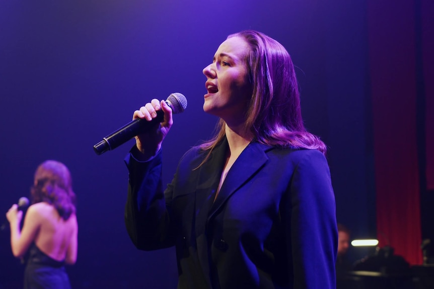 A woman holds a microphone while performing on stage.