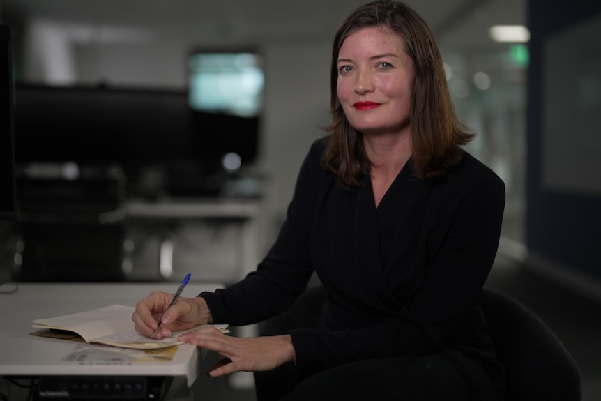A woman sits at a desk and writes.