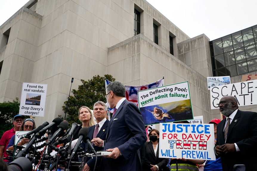 People holding signs in support of David Hearn stand behind him and his legal team at a press conference