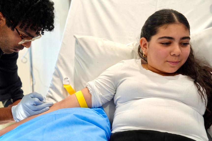 Yasmin Sayed in hospital looks away as a nurse prepares her for a blood transfusion