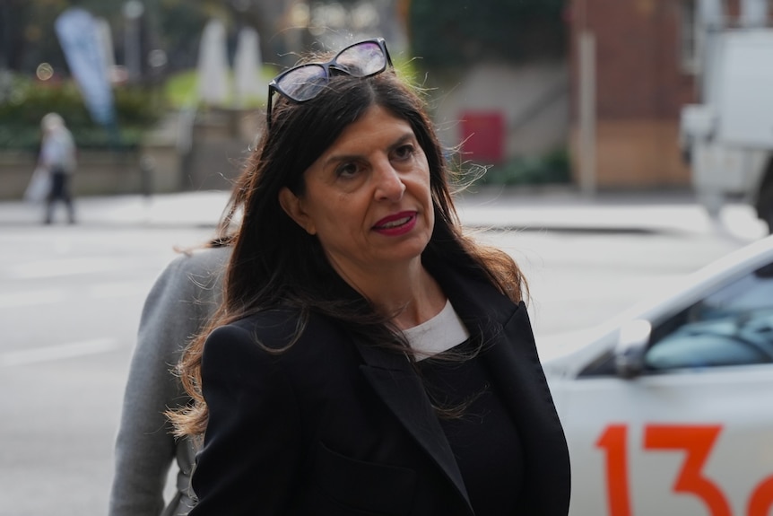 Woman with brown hair wearing black jacket and top in street