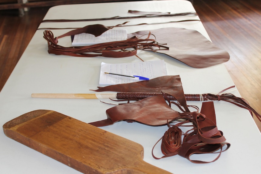 A white table has an open notebook, small timber board, and pieces of leather laying on it.