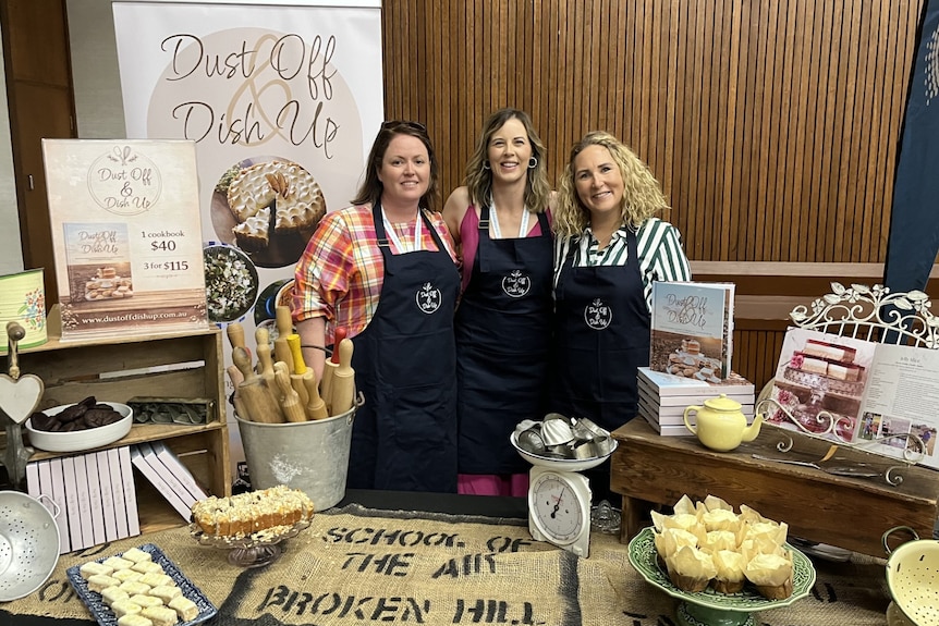 Three women in aprons in front of food