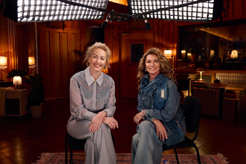 Zan Rowe and Shania Twain seated in a recording studio beneath production lights during a filmed interview.
