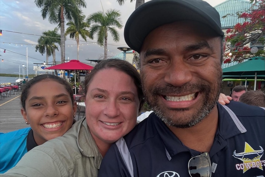 A man takes a selfie with his wife and daughter at a harbour.