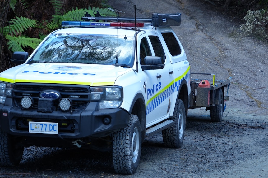 A tasmania police vehicle with a trailer attached is parked in the forest