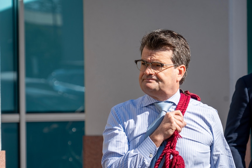 A man in a blue shirt carrying red ropes over his shoulder