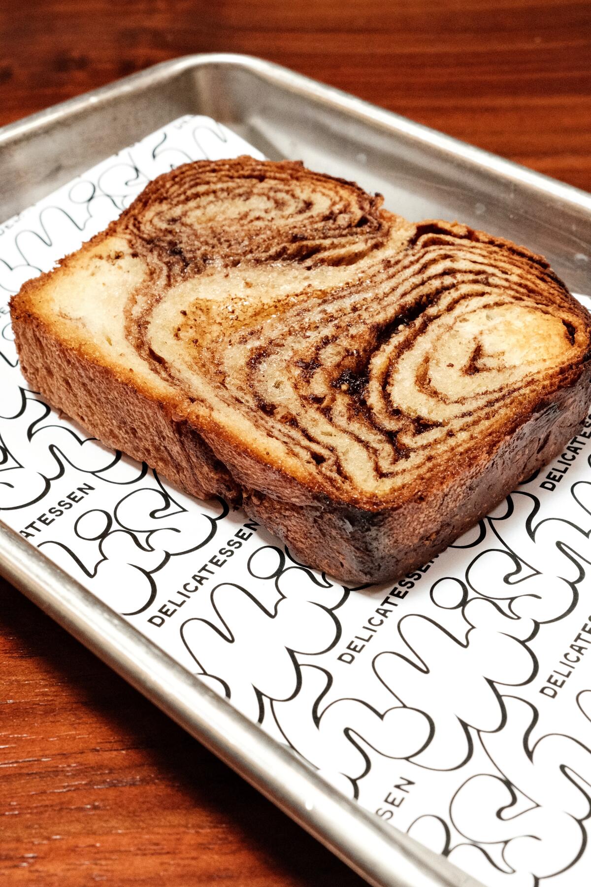 A slice of marbled dark chocolate and hazelnut babka on a silver tray on a wood table