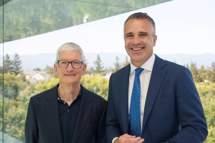 Two men standing next to each other, with green trees behind them