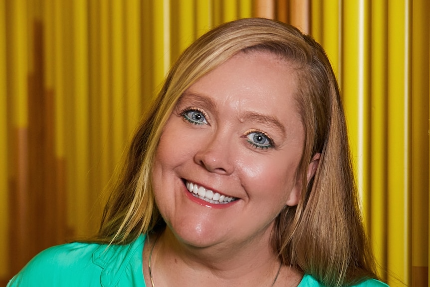 A woman with blond hair and green eyes smiles widely