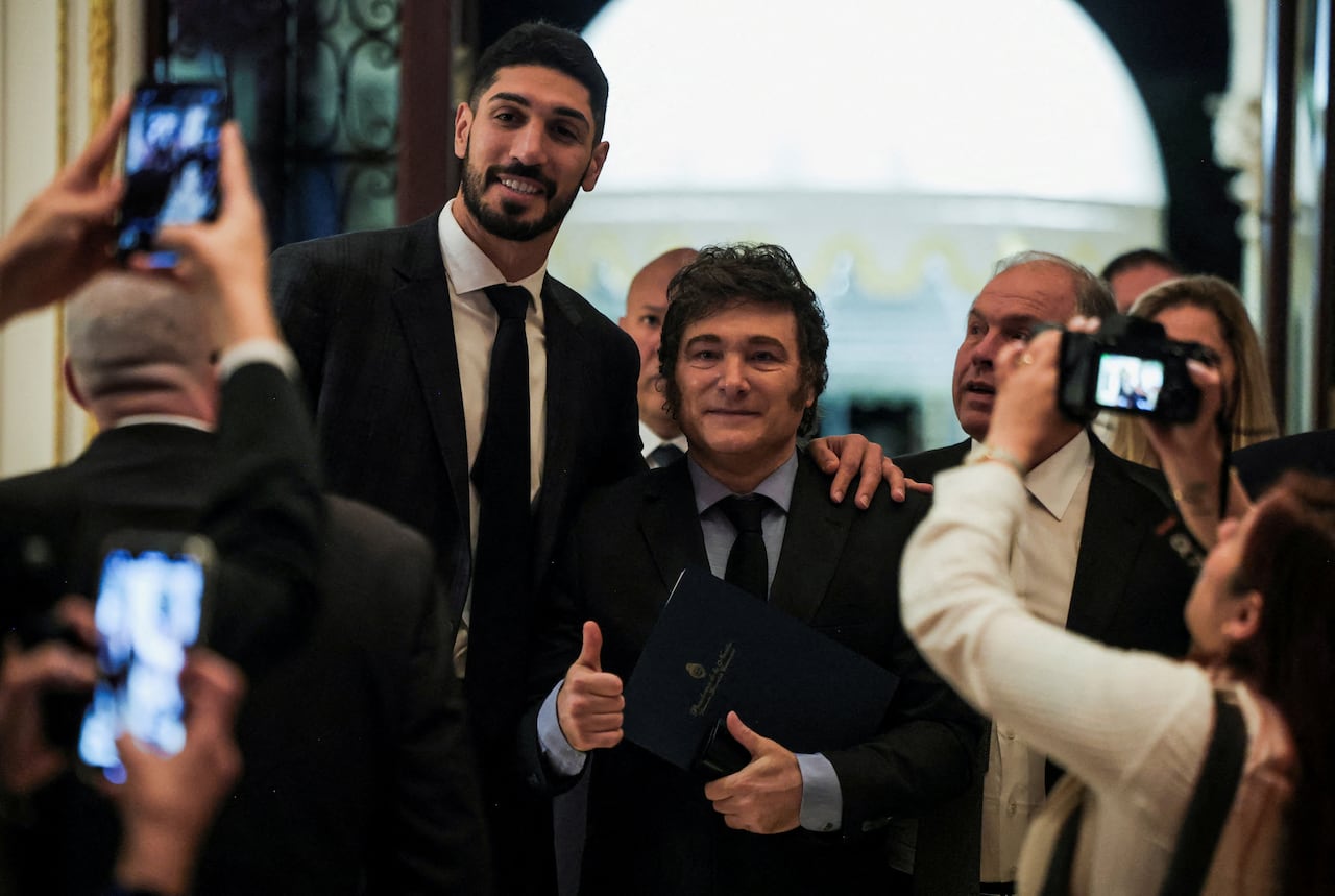 Photographers take photos of two men in suits, holding thumbs up.