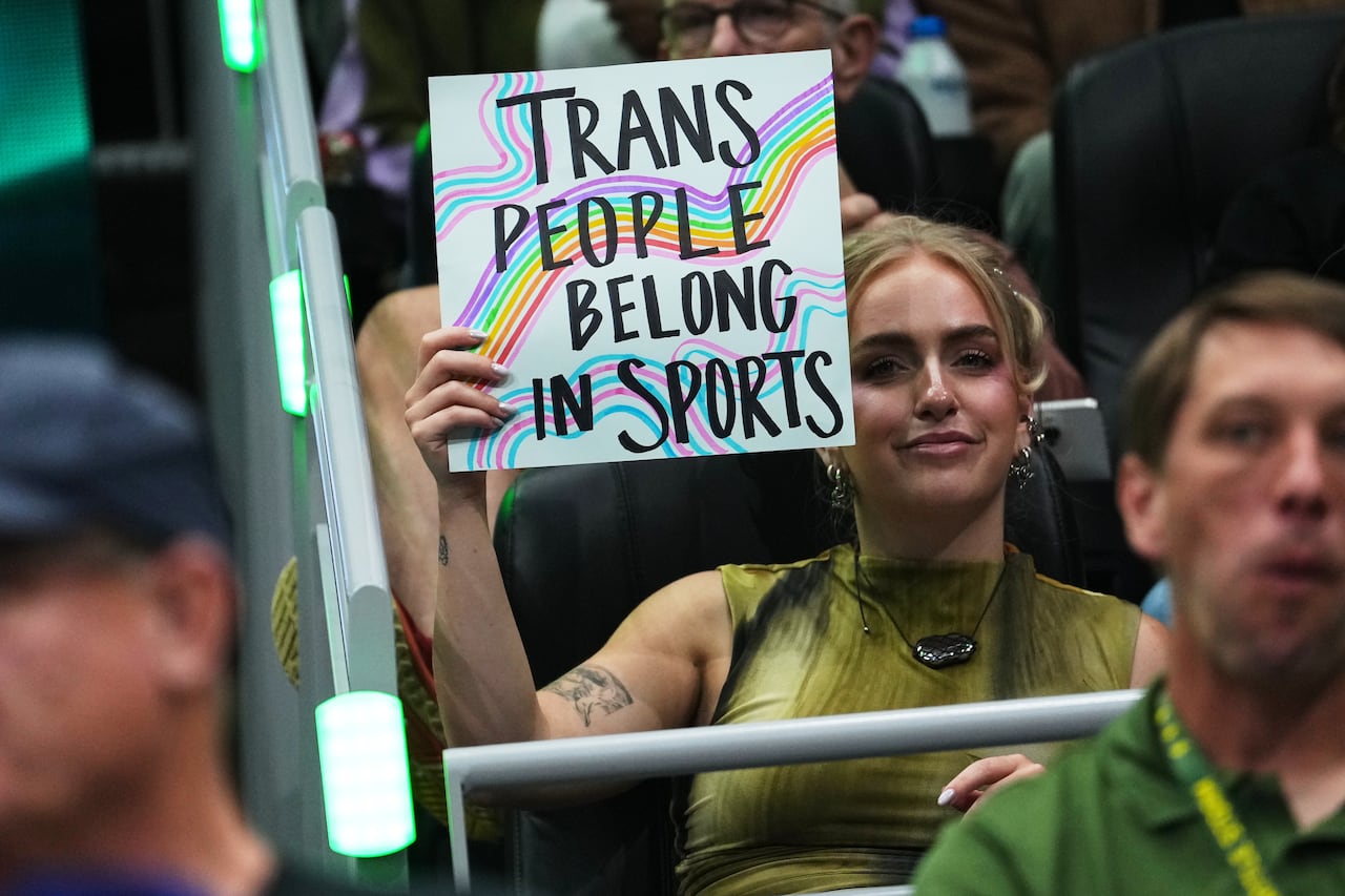 A person holds up a sign that reads, 'Trans people belong in sports.'