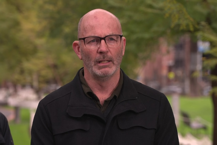 A headshot of a man with a shaved head wearing glasses