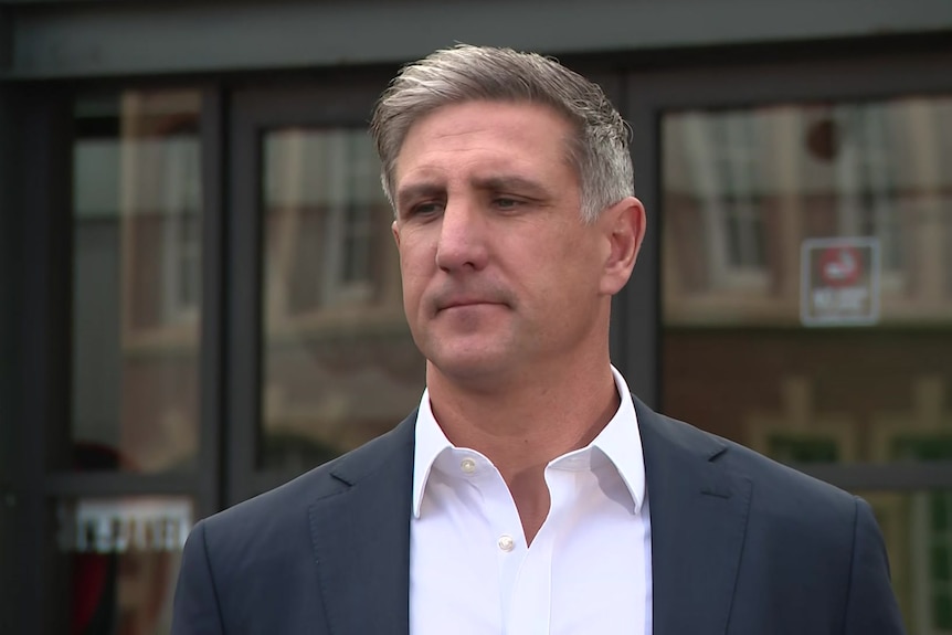 A man with silver hair in a blue blazer and white collared shirt.
