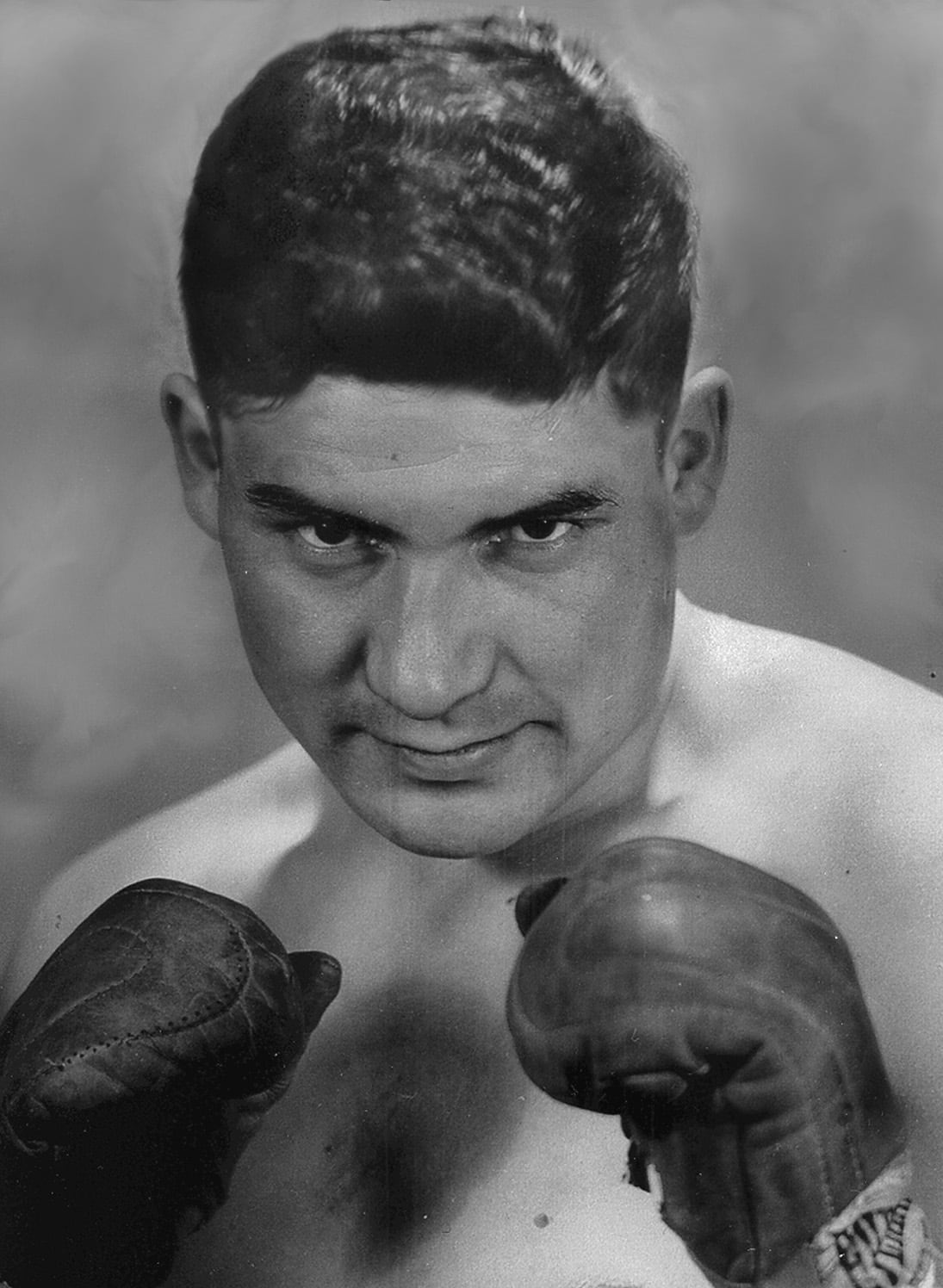 A man looking straight at the camera with boxing gloves. Black and white filter on it