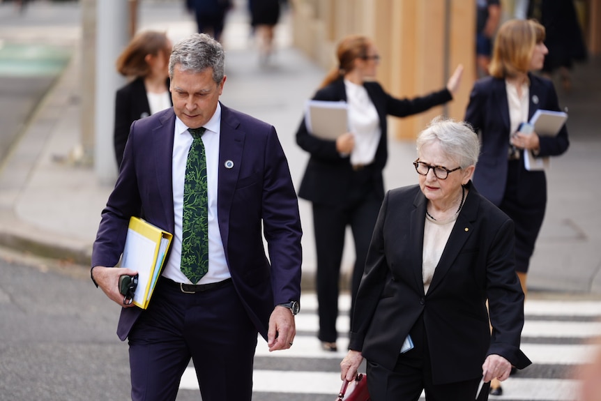Man in suit with documents next to woman carrying a bag.