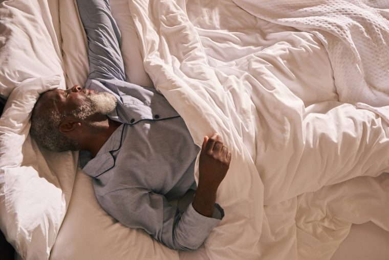 A mature man rouses in the early morning light, stretching as he wakes.