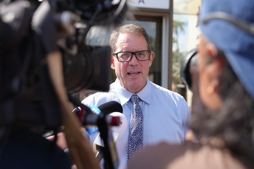 Members of the media surround Luke Gosling speaking outside the courthouse, he is framed between large TV cameras.