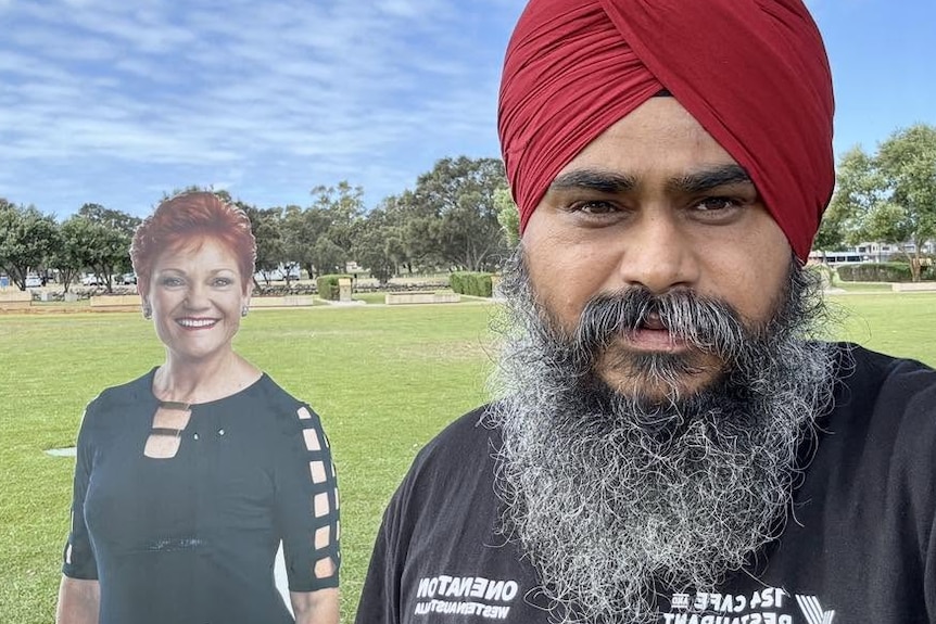 Parminder Singh poses for a photo wearing a red turban, next to a cut-out of Pauline Hanson.