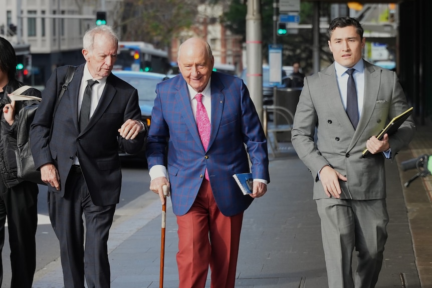 Man in dark blue jacket, white shirt and pink tie walks in other men in suits