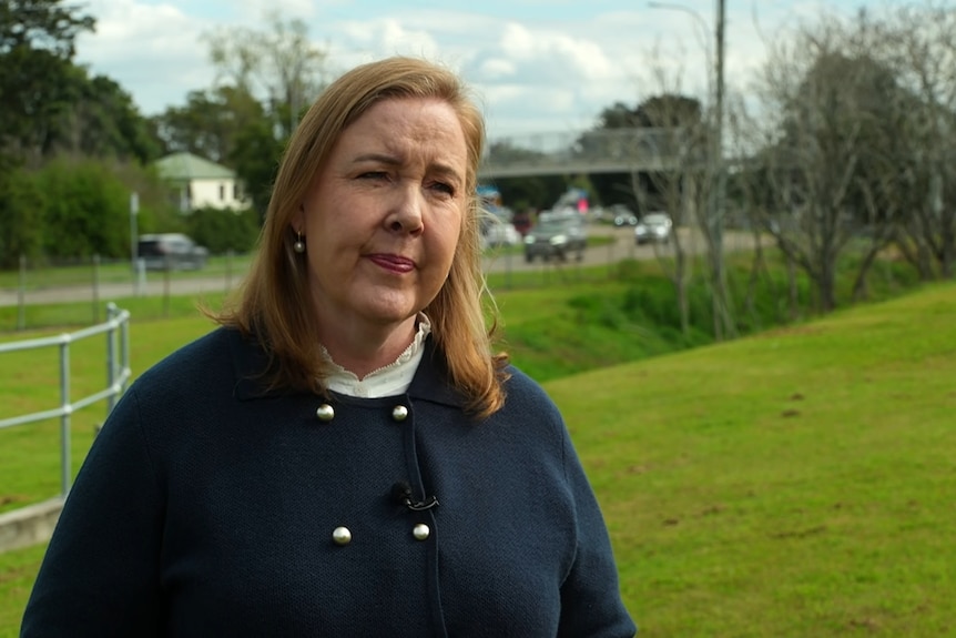 A woman wearing a navy blue jacket stands in front of a busy road