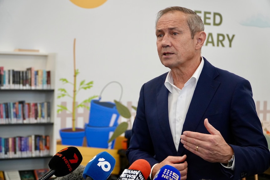 Roger Cook standing right of camera talking into microphones
