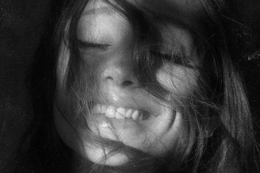 A black and white picture of Ariana Grande with hair covering part of her face; she's smiling.