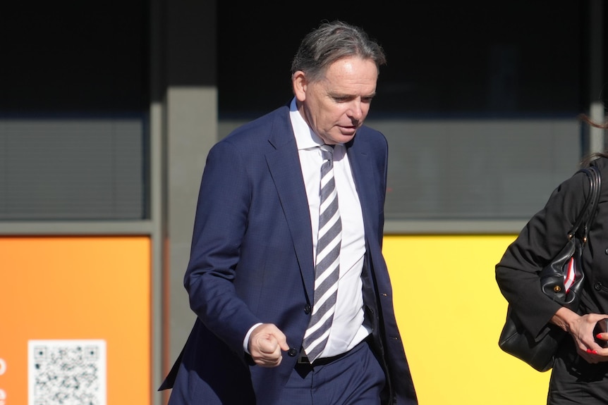 A man in a suit arrives outside a court building.