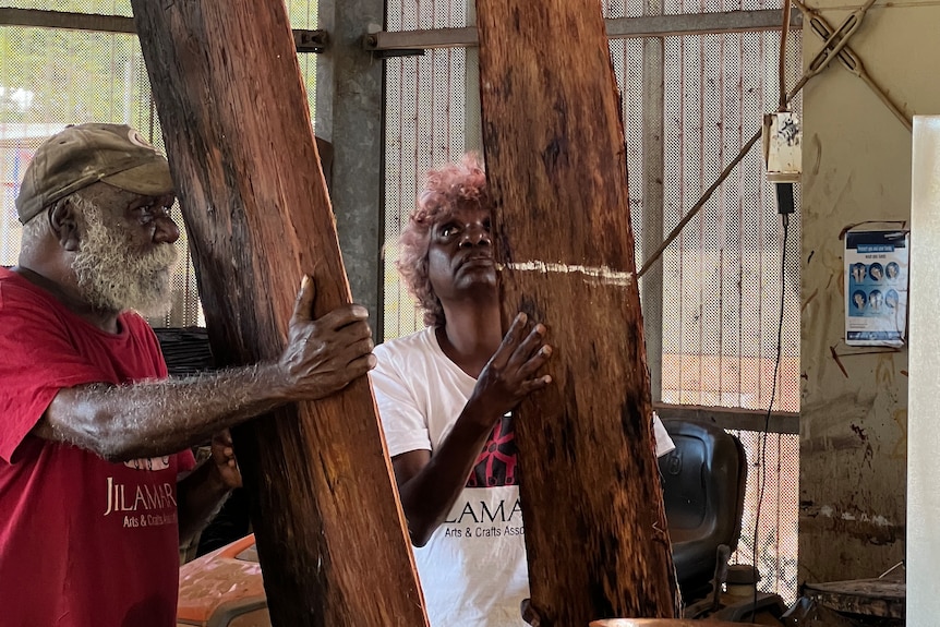 Two artists inside a workshop holding large pieces of bark, the woman is looking up towards the top of her wooden block.