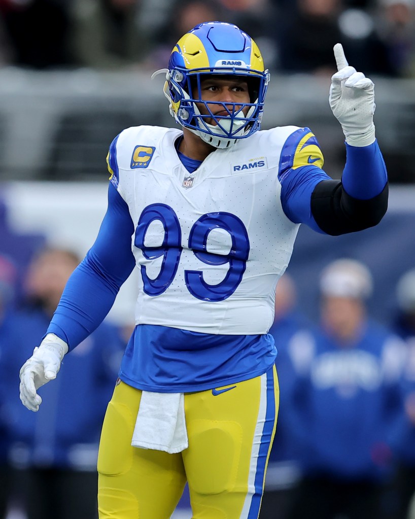 NFL player Aaron Donald of the Los Angeles Rams in a blue and yellow uniform, number 99, with his arm raised and finger pointing.