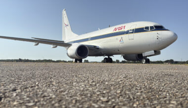A large, white aircraft sits on a concrete surface after being painted with new NASA logos in red, white and blue.
