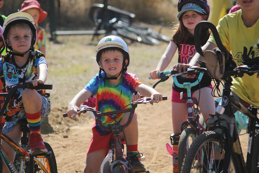 An adult helping push a young girl on a bike with training wheels during a race.