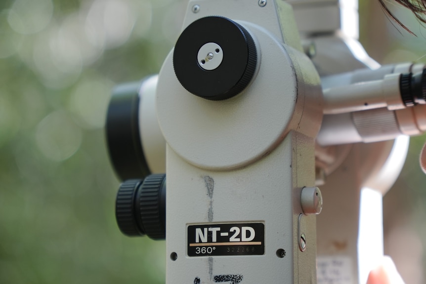 A young woman with a nose-ring looks into the viewing scope of a surveying theodolite.
