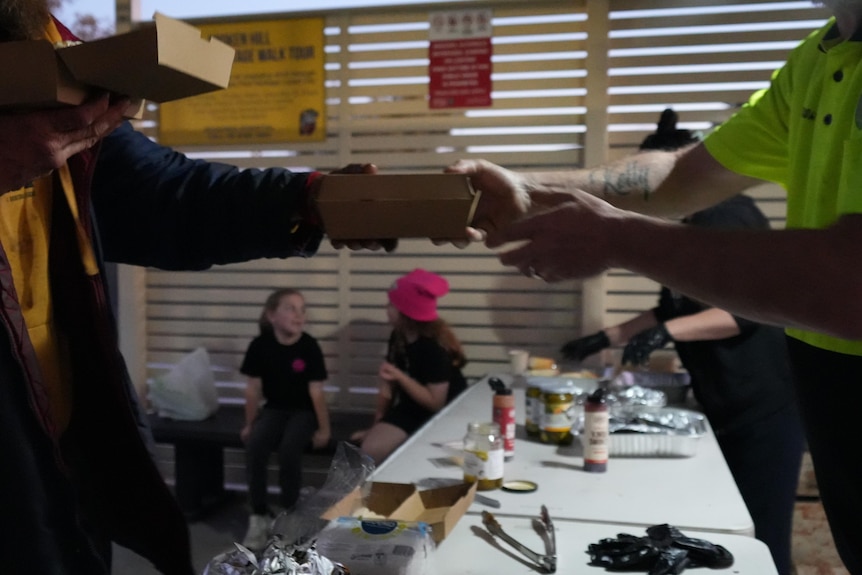 A man handing out a takeaway box with a meal to another man