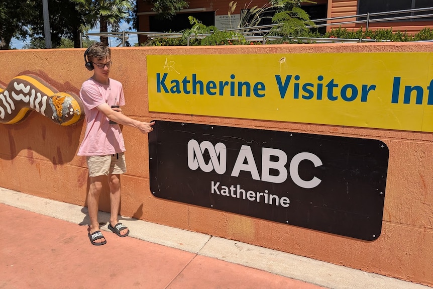 a young man standing in front a sign of ABC Katherine