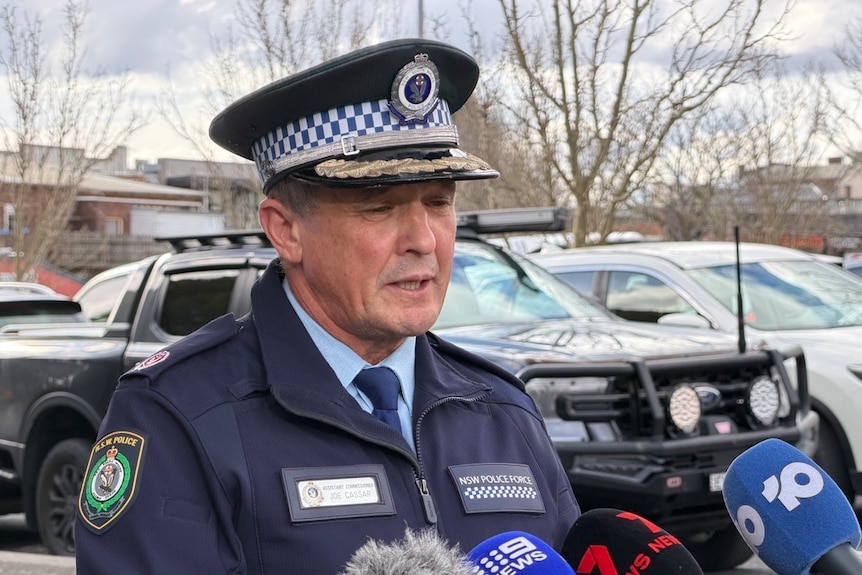 A police commander stands in front of a group of microphones