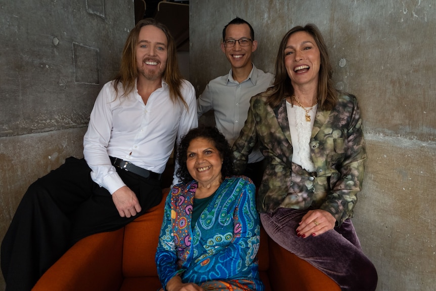 Tim Minchin, Eddie Woo and Claudia Karvan perch on lounge chair arm while Mechelle Turvey is seated. All are smiling.