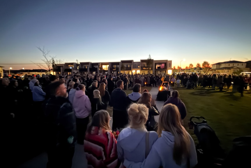 A large group of people attend a vigil at sunset