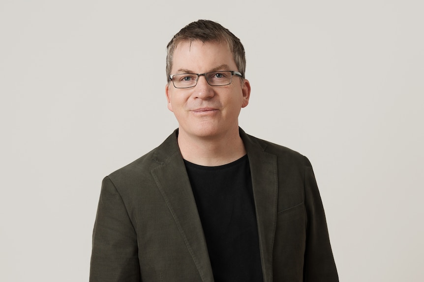 A middle-aged white man wearing a suit jacket over a black t-shirt.