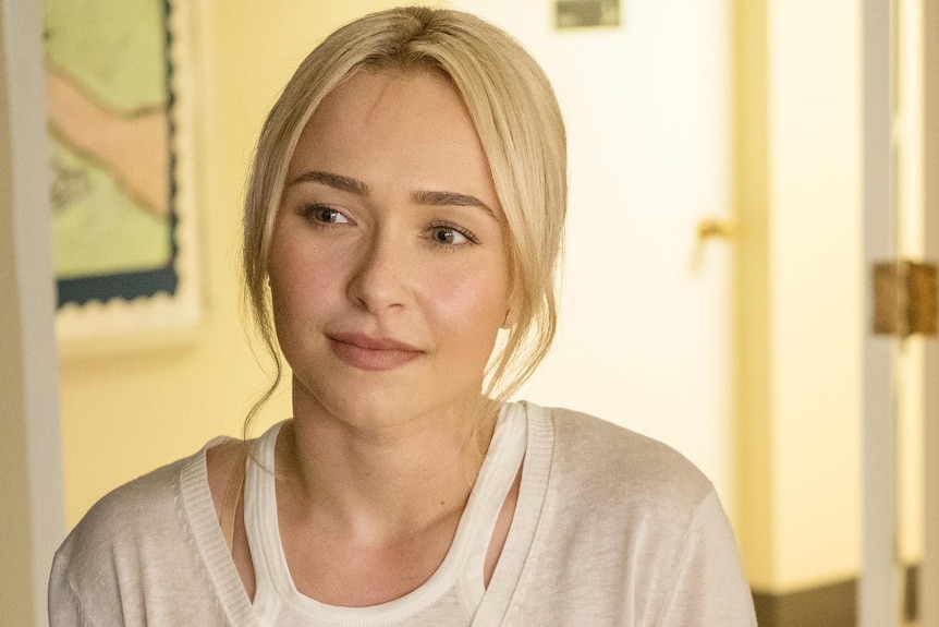 Hayden Panettiere sits smiling, with a white top and her blonde hair tied back.