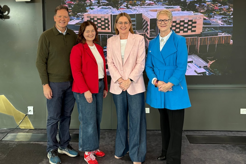 A man stands with three women in front of a large picture of a hospital.