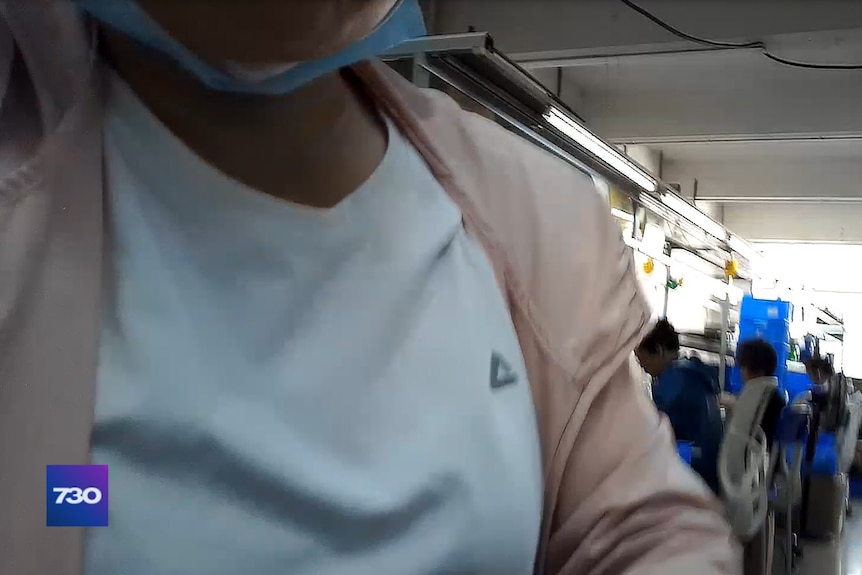 A worker's chest and shoulders can be seen in a factory.