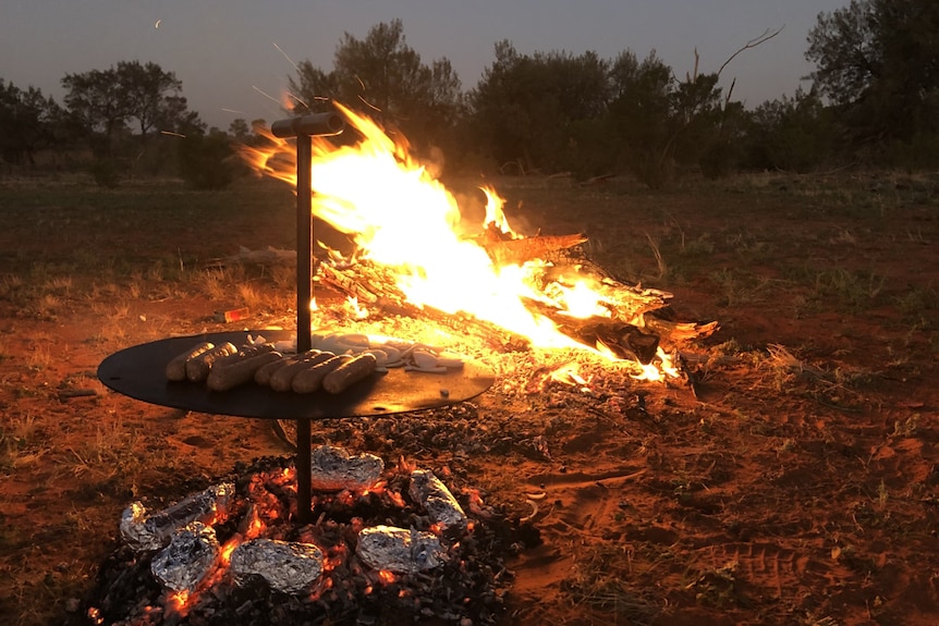 sausages cook next to an outdoor campfire