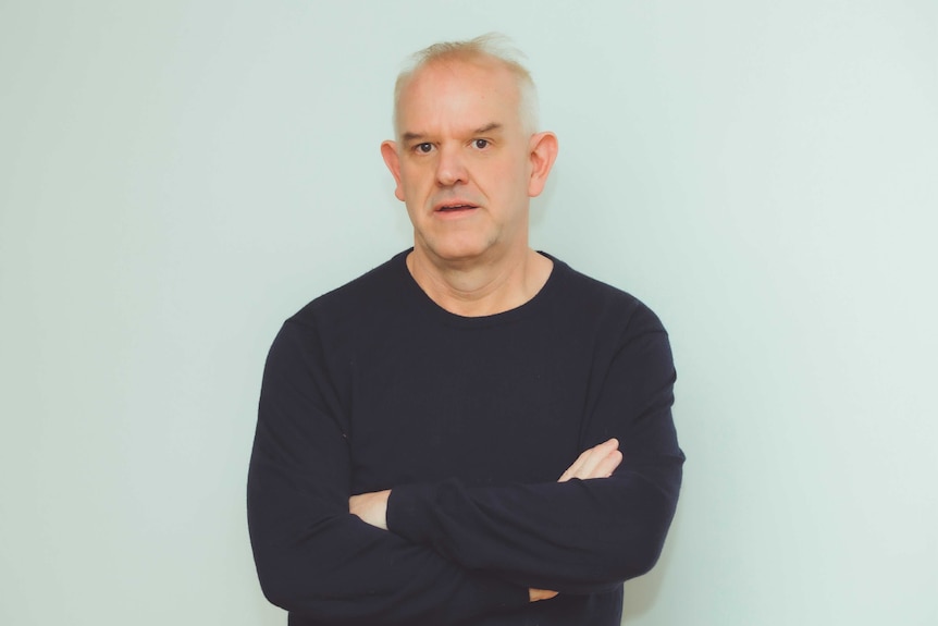 A man wearing a dark sweater with his arms folded in front of him. 