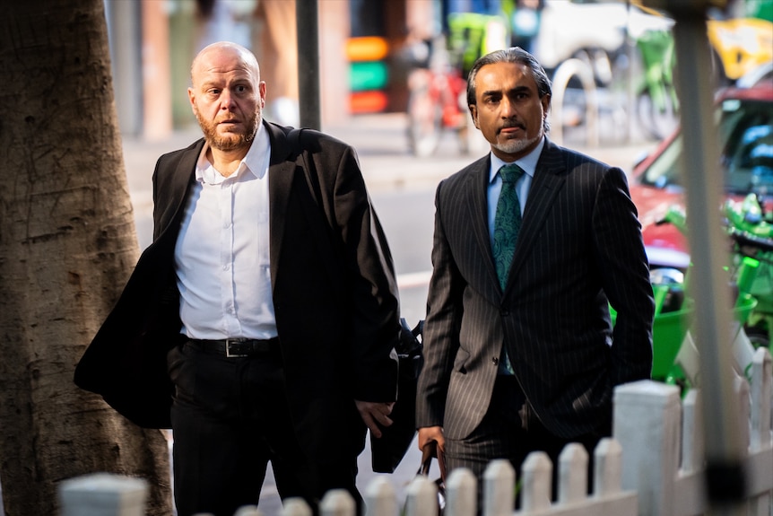 Sheikh Alsuleiman in a black blazer and pants with a white longsleeve walking on a street path.