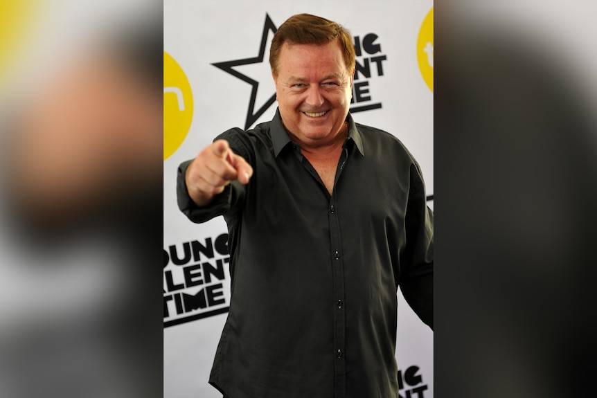 A man wearing a black shirt points to the camera with his index finger.
