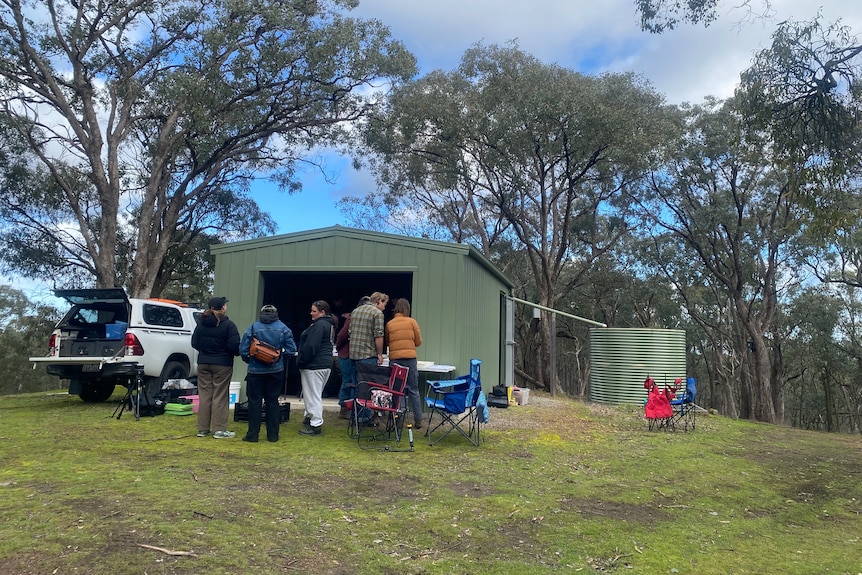 A handful of people standing around a shed. 